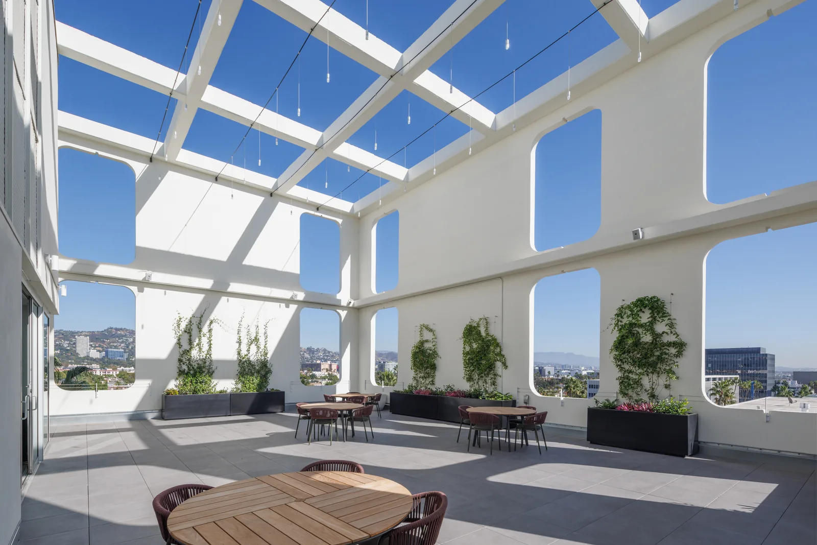 Rooftop terrace set with dining tables under an open pergola, city views beyond